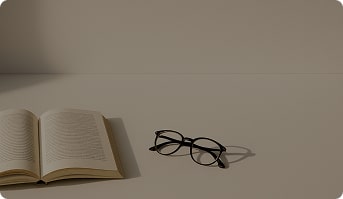 Minimalistic composition with a neutral background, soft shadows from a book and a pair of glasses on a clean desk. Light aesthetic with space for adding text on top