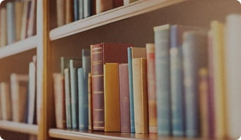 A softly blurred bookshelf filled with colorful book spines, warm ambient lighting, and a shallow depth of field. Suitable as a background image for homepage banners.